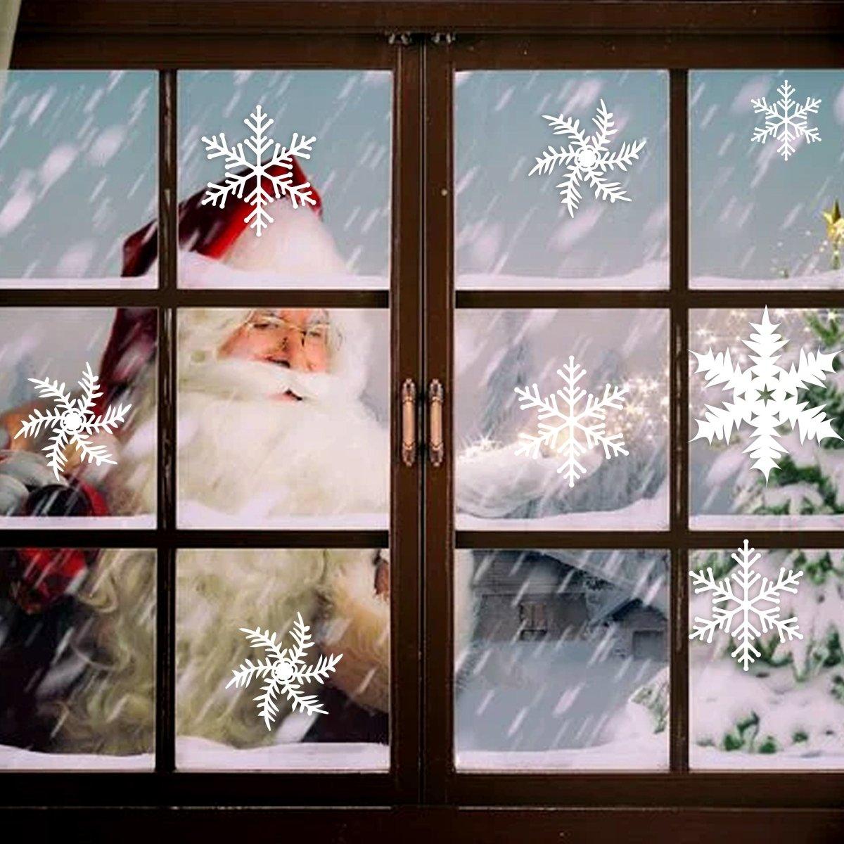 Santa Claus behind window decorated with large snowflake stickers during snowfall, creating a festive Christmas scene.
