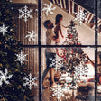 Festive family decorating a Christmas tree through a window adorned with snowflake stickers.