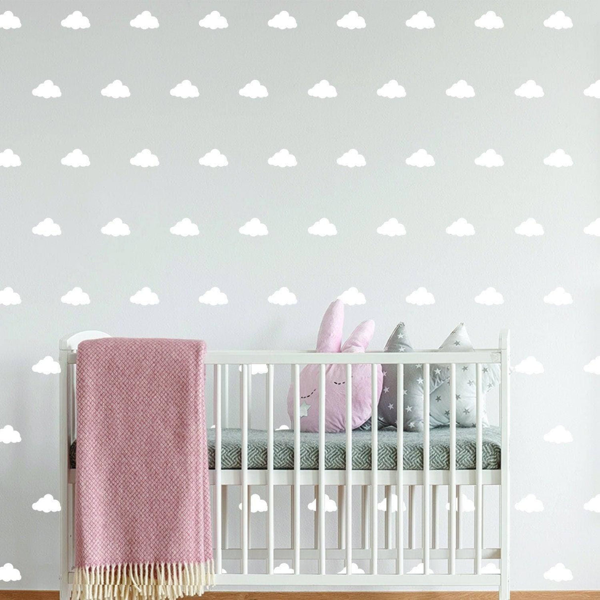 WhimsiCloud children's wall stickers in a nursery with a crib, pink blanket, and plush toys against a cloud-filled wall.