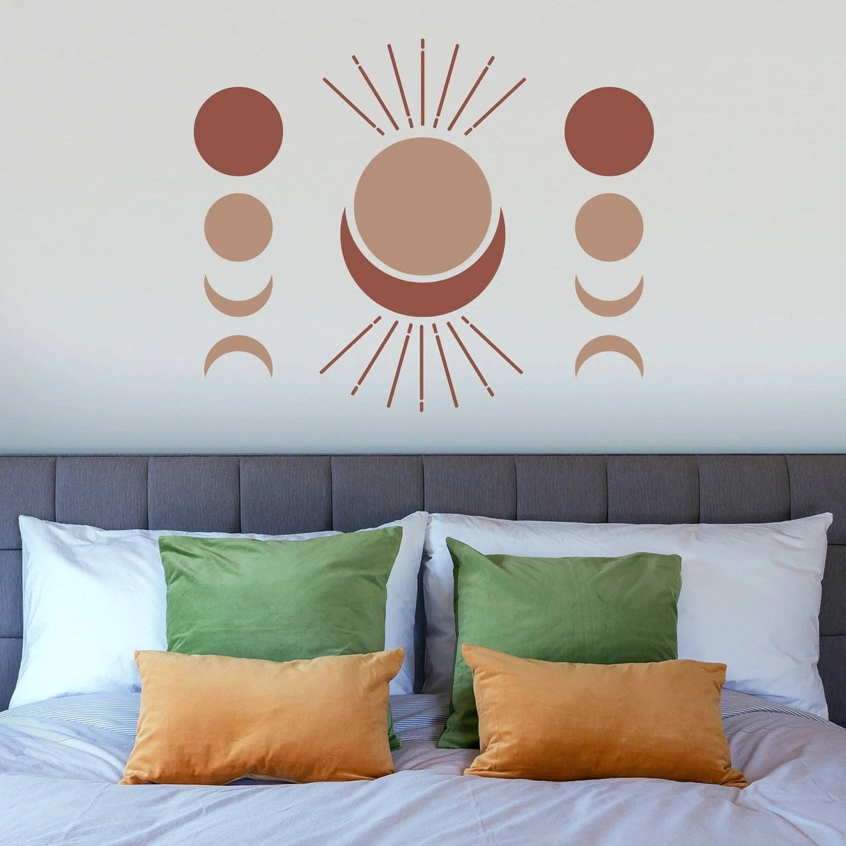 Bohemian crescent and moon phases wall art decal above green and orange pillows on a bed.