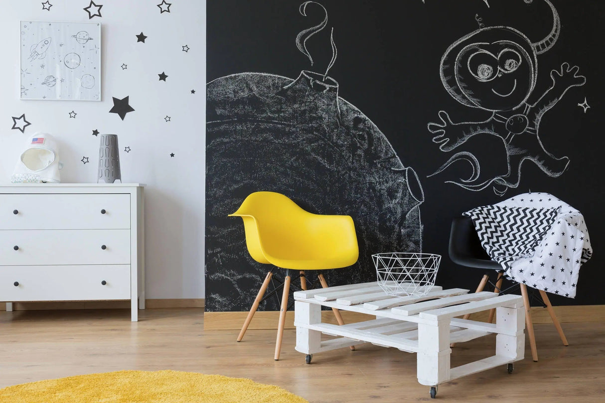 Colorful child's room featuring chalkboard wall decals, including stars and an astronaut, with yellow and black chairs.