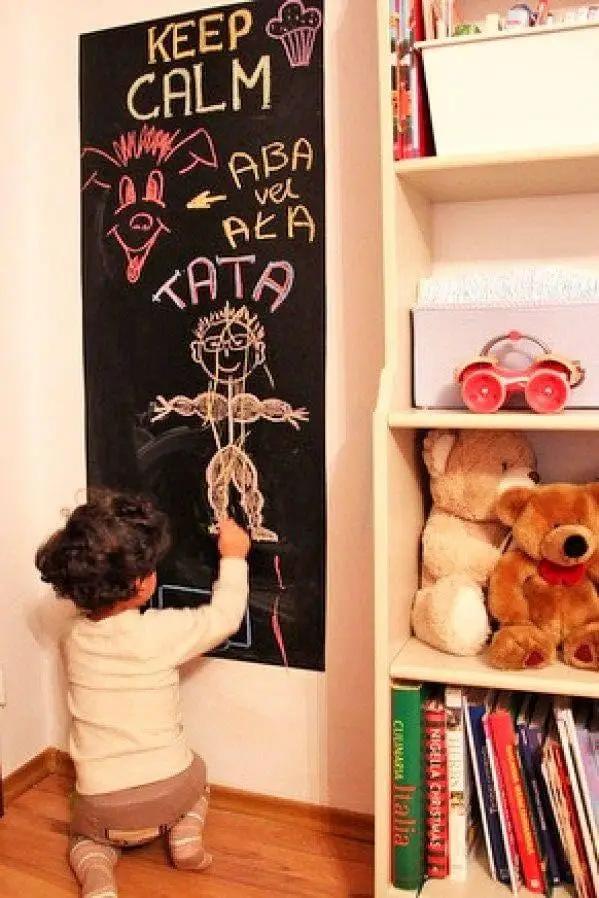 Child drawing on reusable chalkboard wall decal in a cozy room with toys and books.