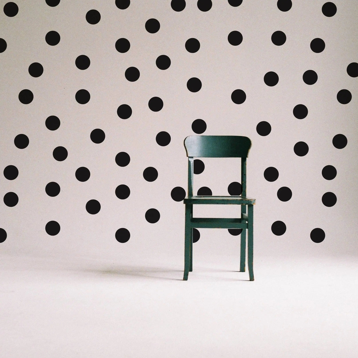 Green chair against a wall decorated with black circle wall stickers, creating a playful and creative space.