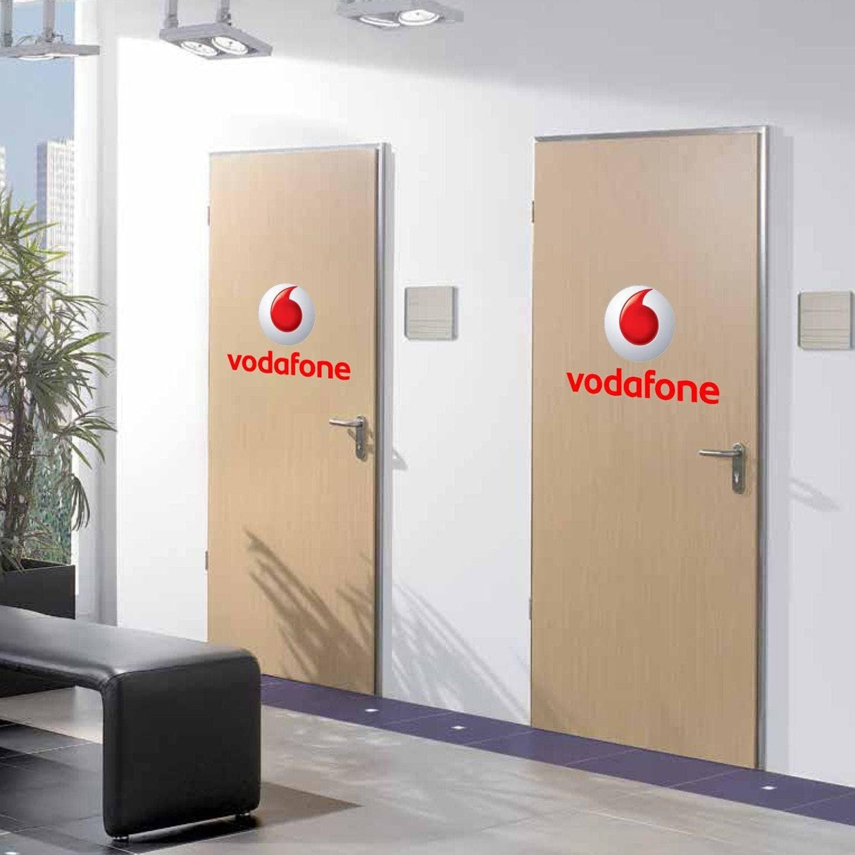 Two office doors featuring Vodafone logo decals on a modern office wall.