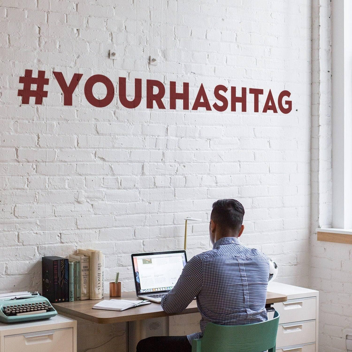 Custom vinyl hashtag decal displayed on a wall above a desk with a person working on a laptop.