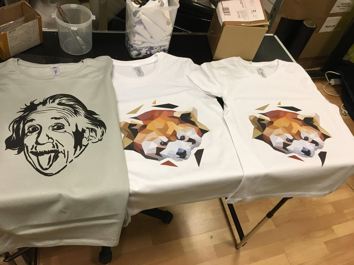 Custom t-shirts featuring an Einstein graphic and a stylized dog design on display in a creative workspace.