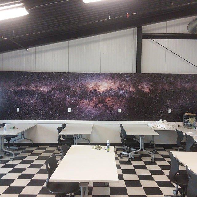 Classroom with a cosmic-themed wall mural featuring a galaxy, complemented by modern desks and chairs.