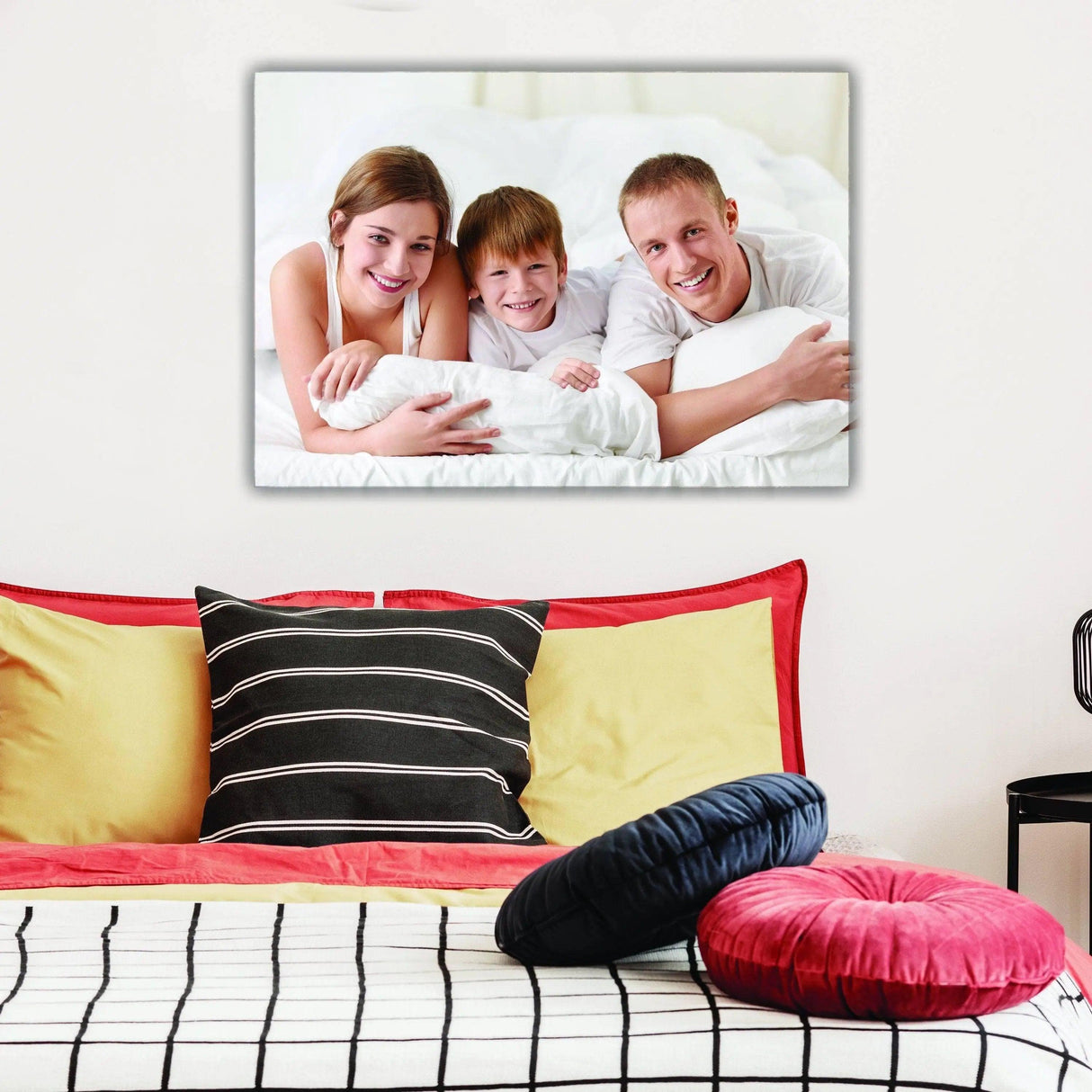 Family portrait canvas print on wall above colorful pillows in a cozy bedroom setting.