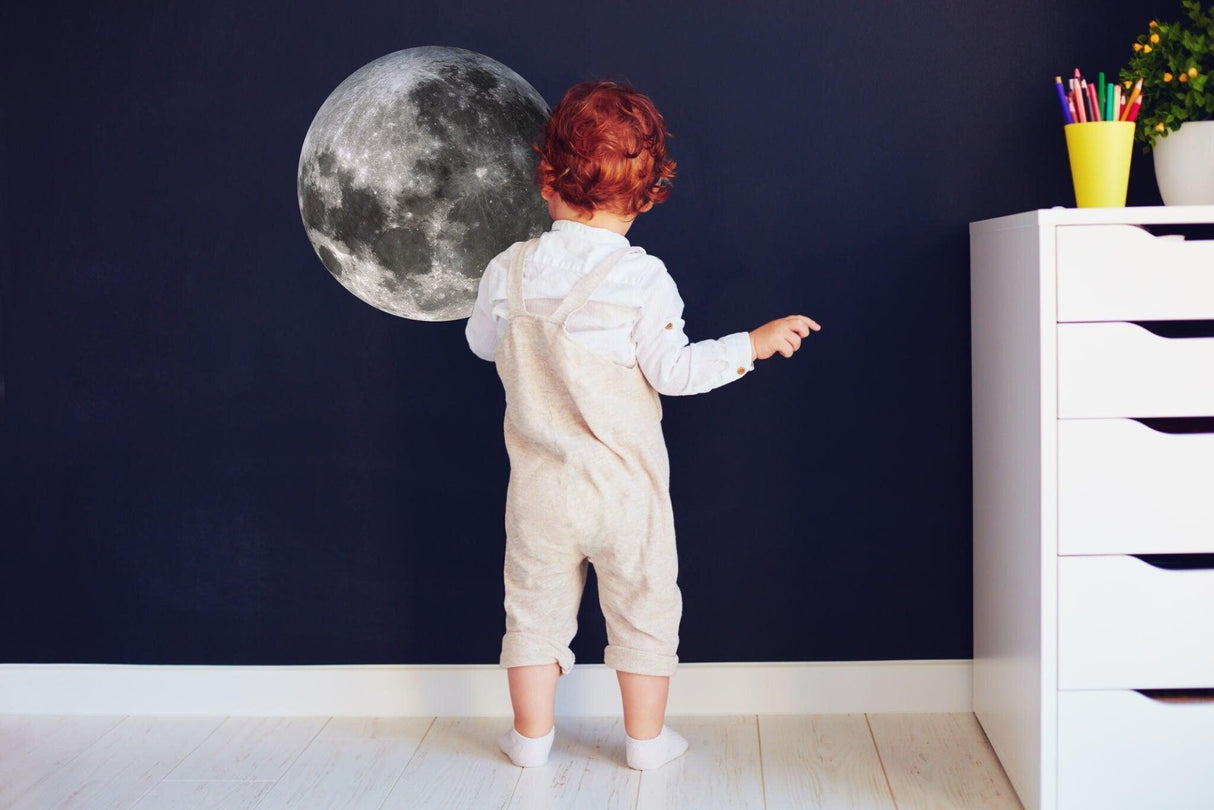 Child admiring a large moon wall sticker in a stylish room, enhancing a celestial theme.