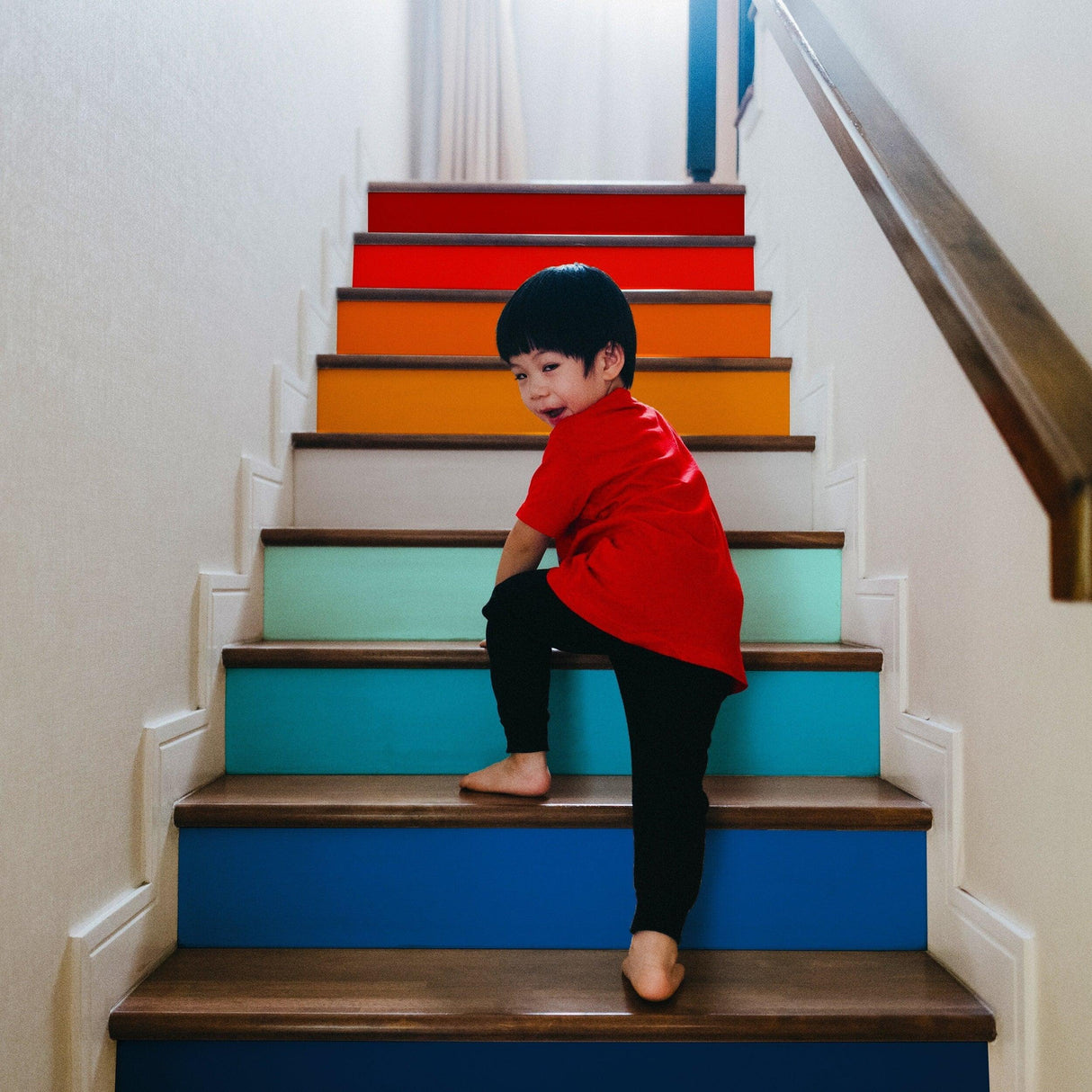 Child climbing colorful gradient stair risers with vibrant stickers for a playful staircase makeover.