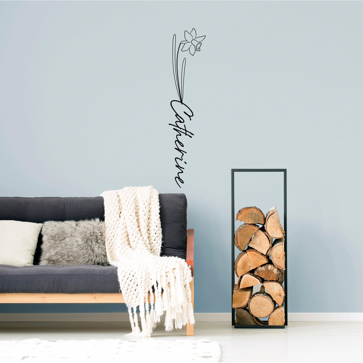 Personalized birth flower decal with name 'Catherine' above a cozy sofa in a stylish living room.