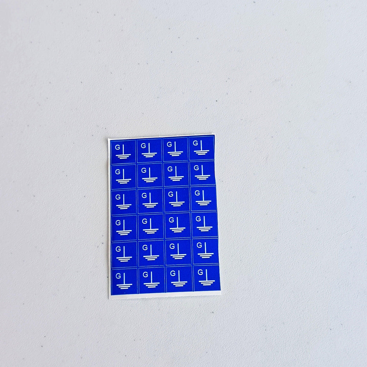 Sheet of 24 blue grounding symbol stickers with square 'G' labels for electrical safety.