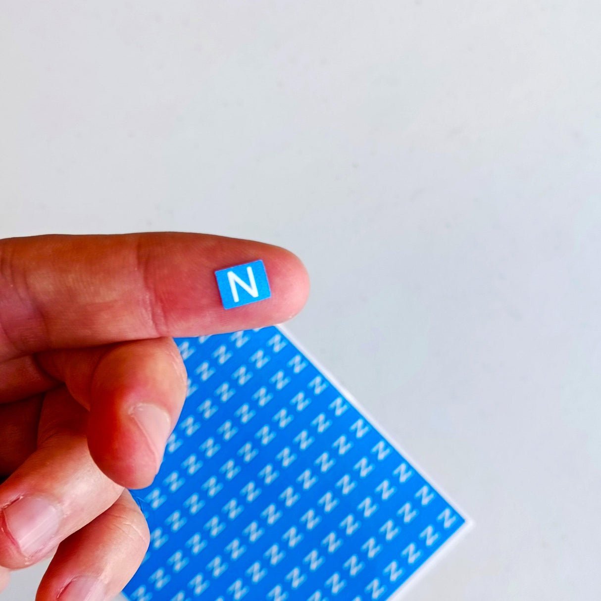 Hand holding a blue 'N' sticker from a sheet of neutral marking labels for electrical safety.