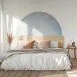 Minimalist blue half-circle wall decal above a modern bed with neutral bedding and wooden headboard in a Scandinavian bedroom.