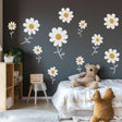 Bright nursery decorated with white daisy wall decals on a dark wall, featuring a teddy bear on the bed.