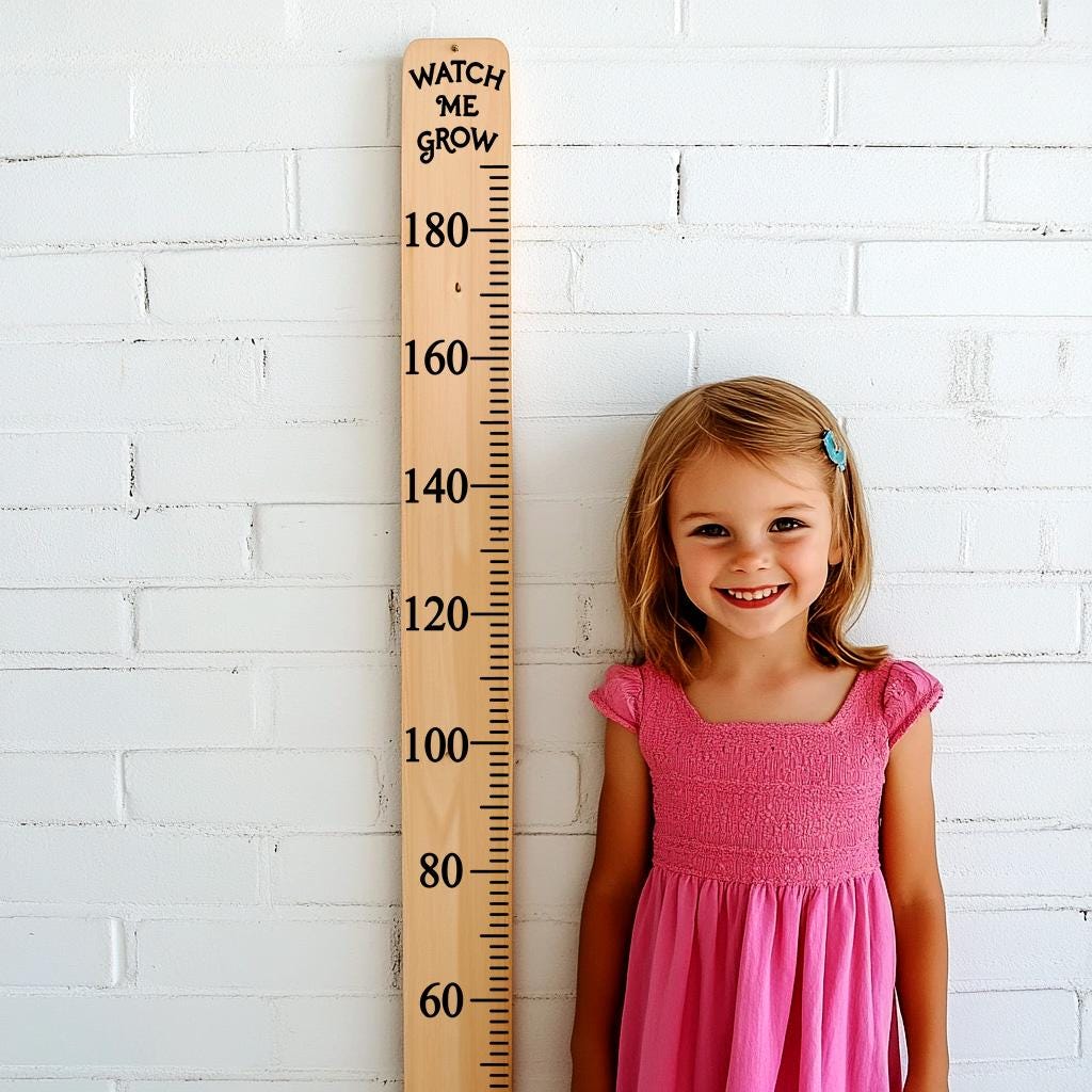 Girl smiling next to a wooden growth chart ruler for tracking height progression.