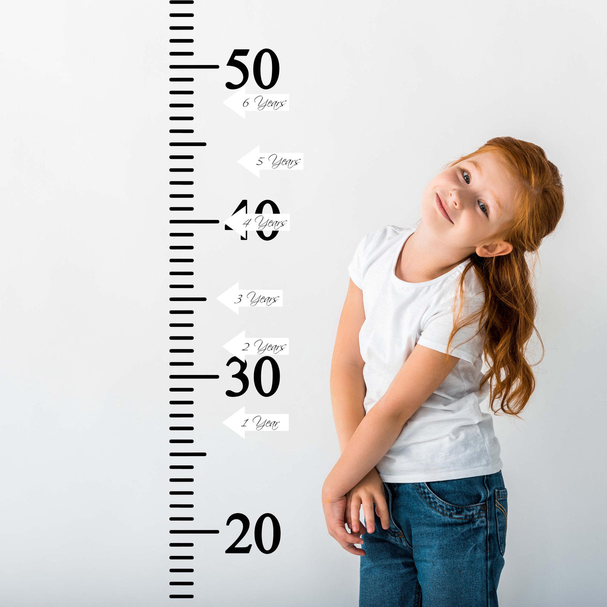 Child posing next to a vinyl growth chart ruler wall decal, measuring height in inches, with arrow stickers for milestones.