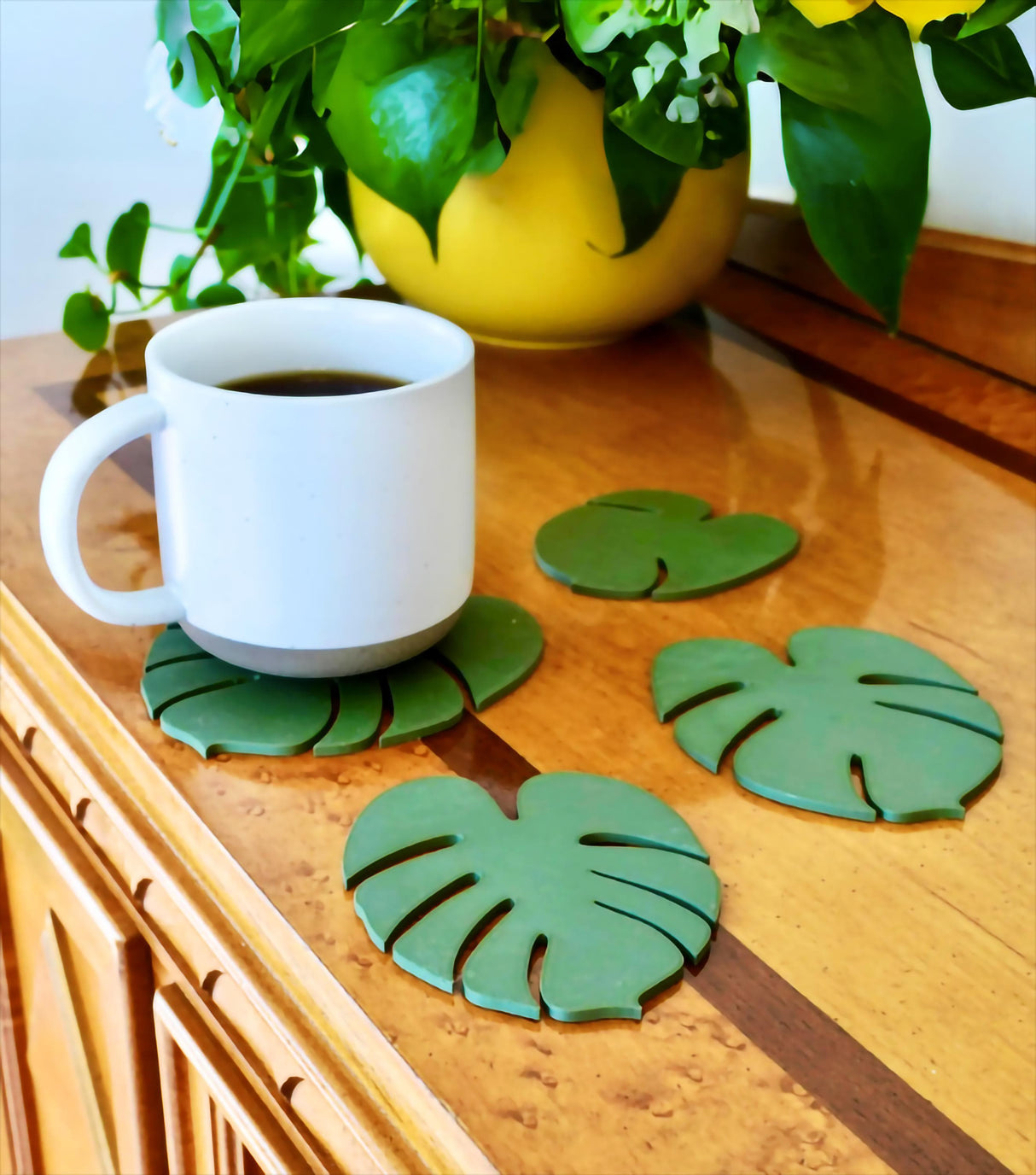 Monstera leaf coasters on a table with a white mug and plant, showcasing stylish home decor.