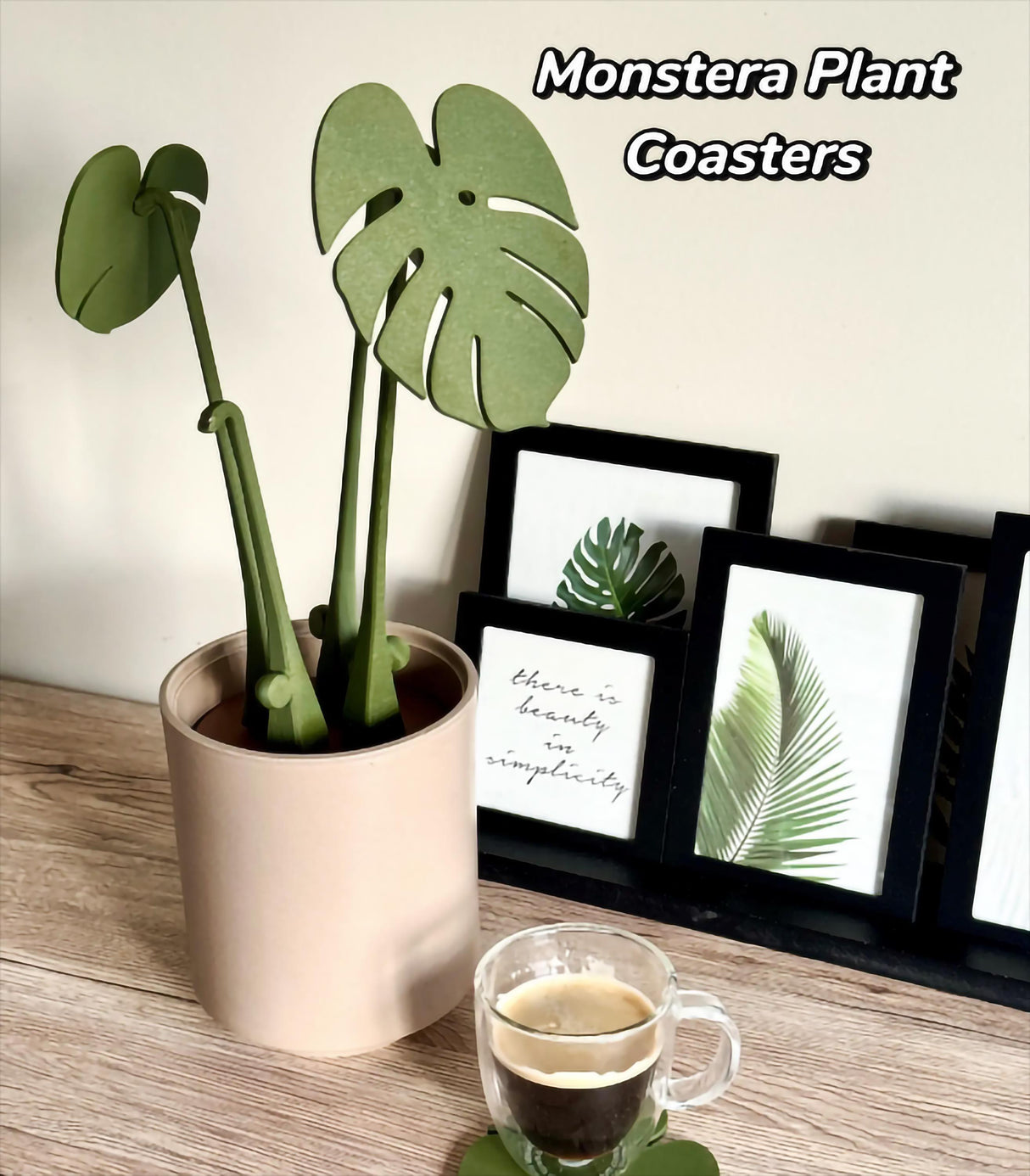Monstera leaf coasters in a planter beside framed plant art and a coffee cup on a wooden surface.