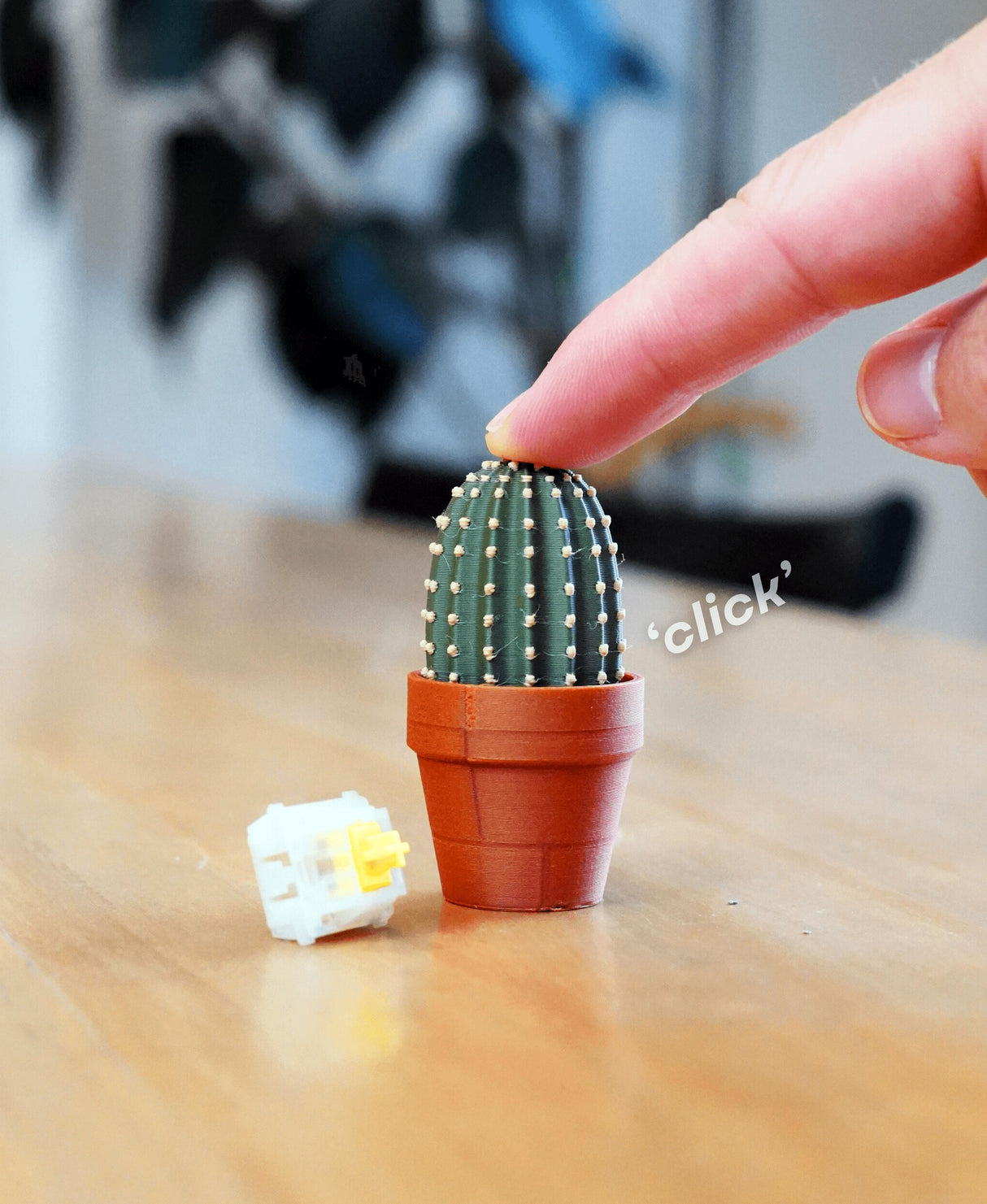 Finger pressing a mini clickable cactus toy on a desk, showcasing its mechanical fidget design and stress-relief feature.