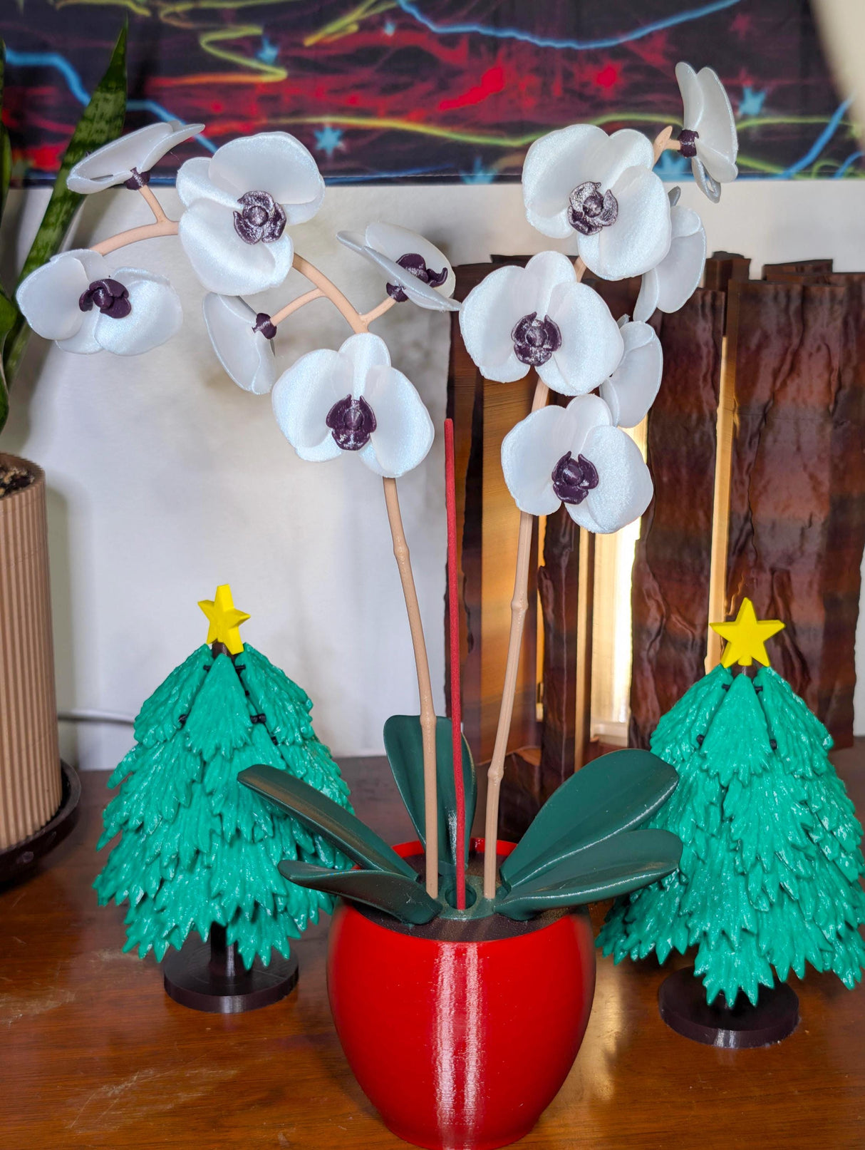 Aromatic orchid oil diffuser in a red pot with green fan leaves, surrounded by Christmas tree decor.