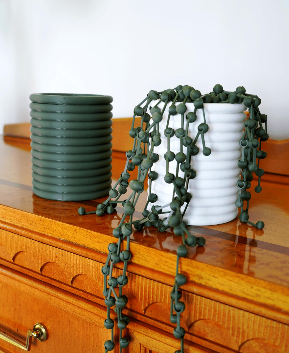 String of Pearls faux plant cascading over white pot next to green pot on wooden surface