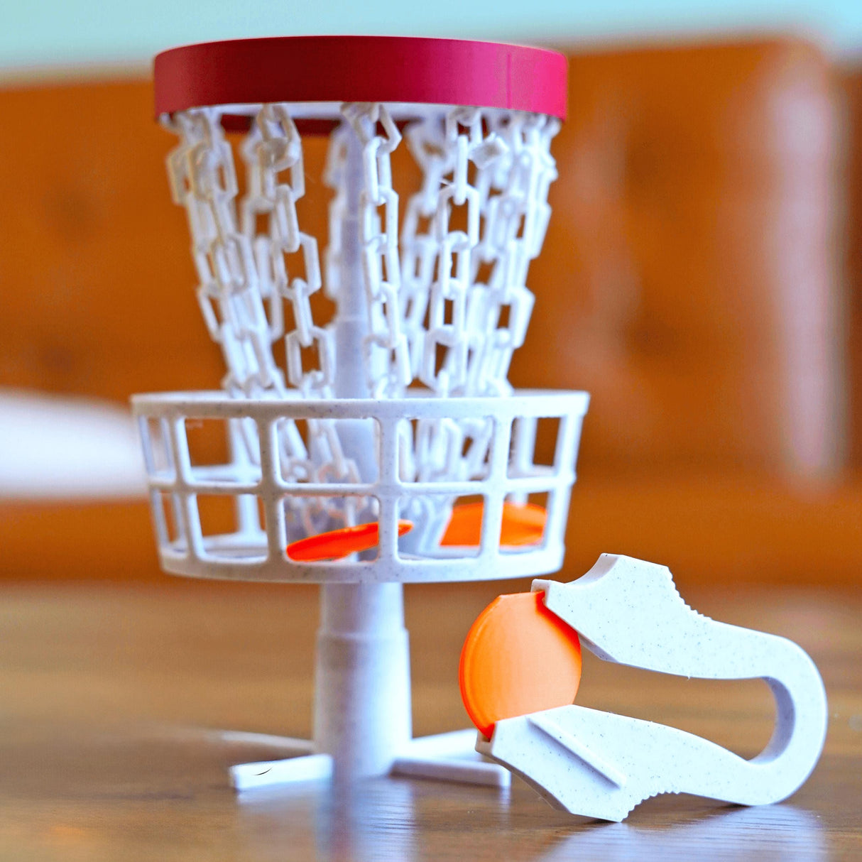 Mini disc golf basket with chains and an orange disc, perfect for desk trick shots and office fun.