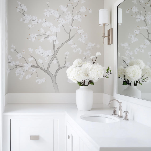 Chinoiserie tree wall decal with white flowers in a light gray bathroom, featuring a modern sink and vase of hydrangeas.