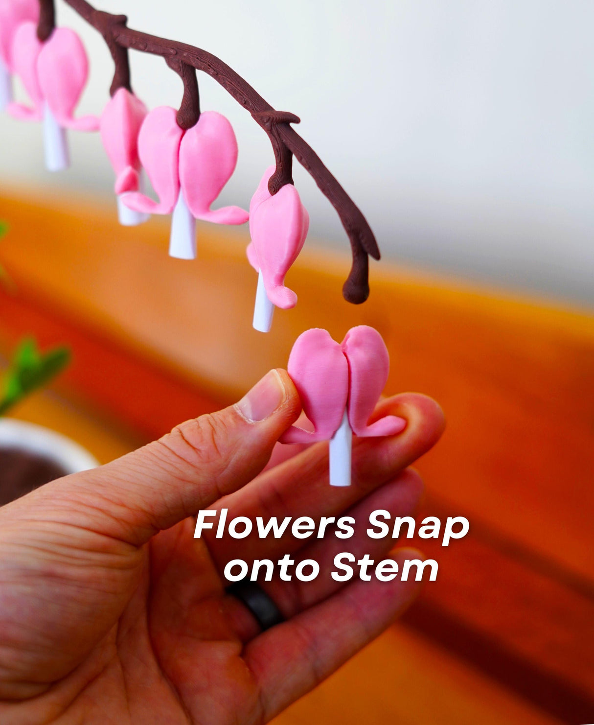 Hand holding a pink bleeding heart flower, showcasing how flowers snap onto the decorative stem.