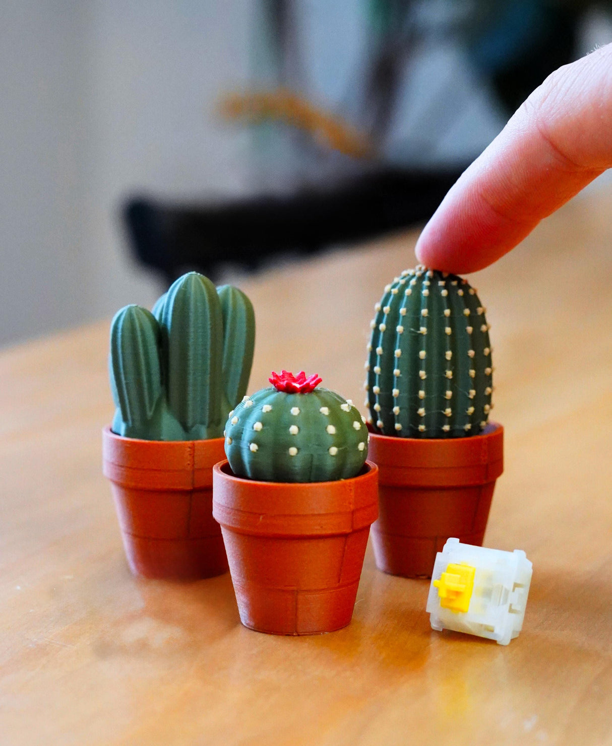 Mini Clickable Cacti in pots, showcasing a finger pressing the textured cactus for fidget fun and desk decor.