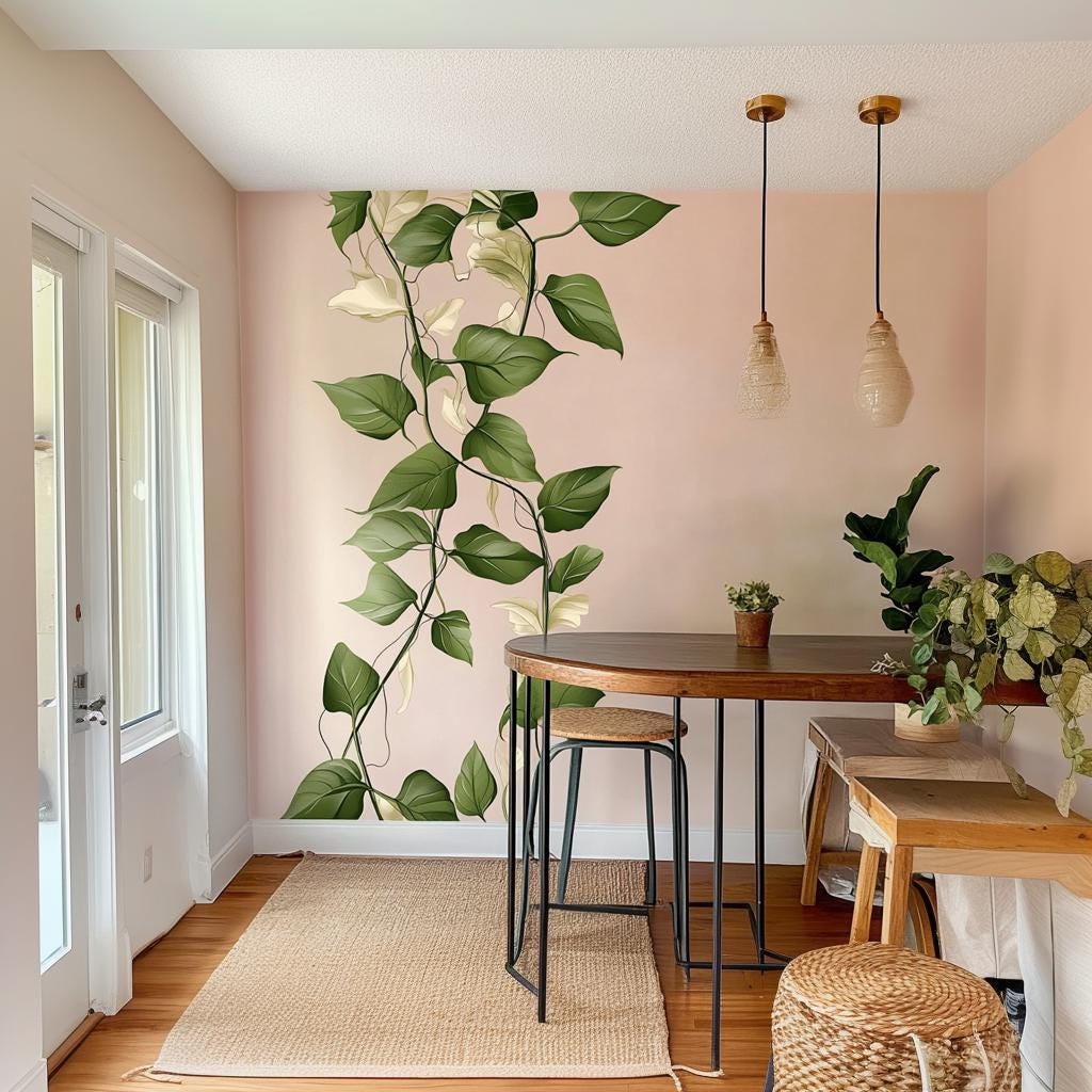 Climbing vine wall decal sticker with green leaves and cream accents on a pink wall in a cozy dining space.