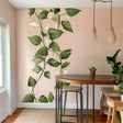 Climbing vine wall decal sticker with green leaves and cream accents on a pink wall in a dining space.