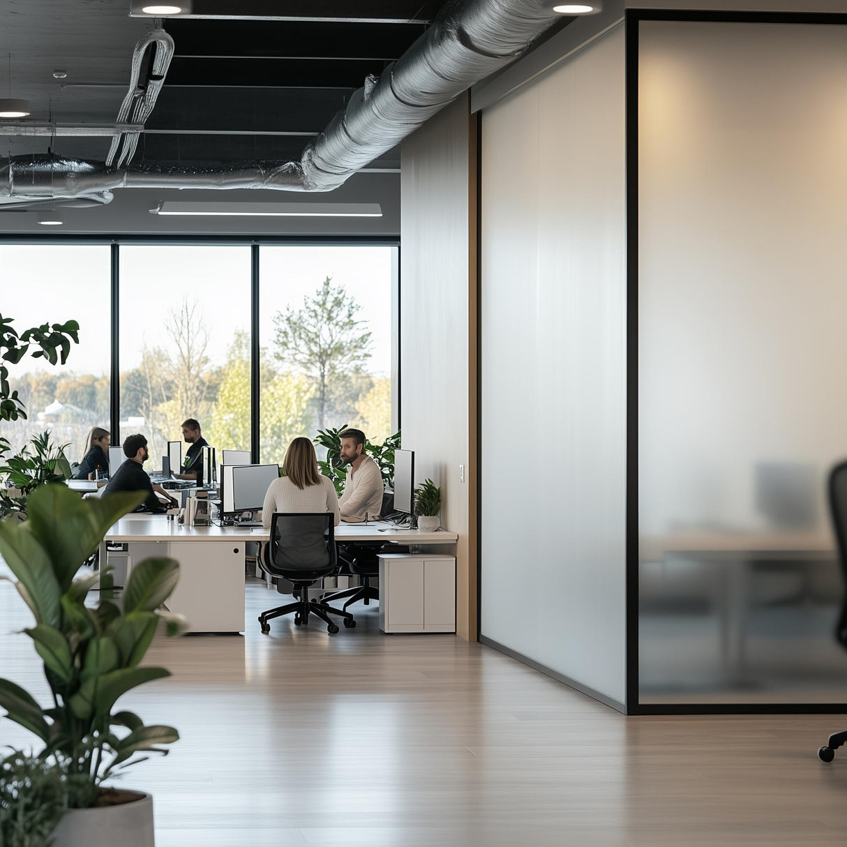Modern office space with frosted glass partitions and people working at desks, enhanced by natural light.