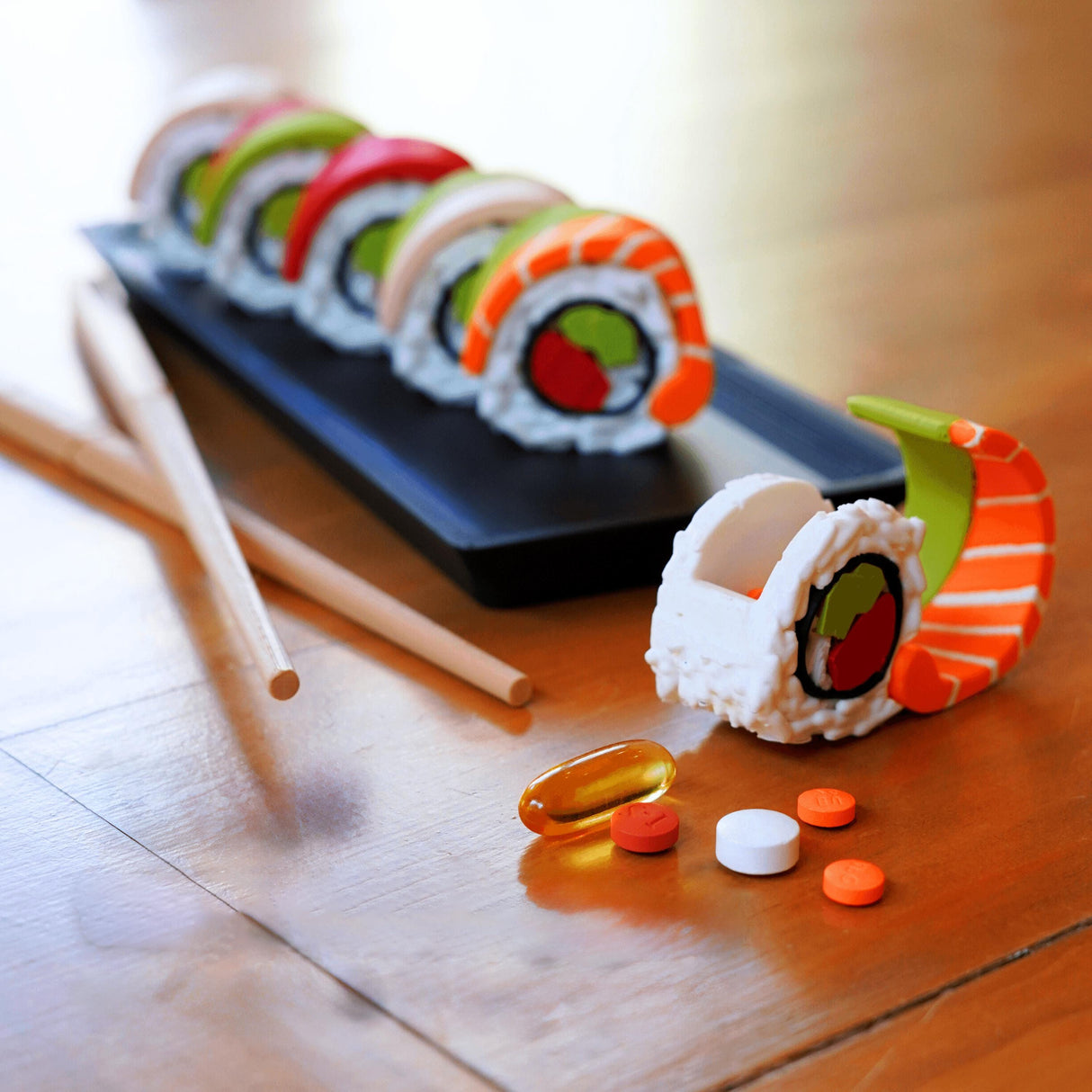 Colorful sushi pill organizer set on a black tray with pills and chopsticks, perfect for sushi lovers and weekly supplement management.
