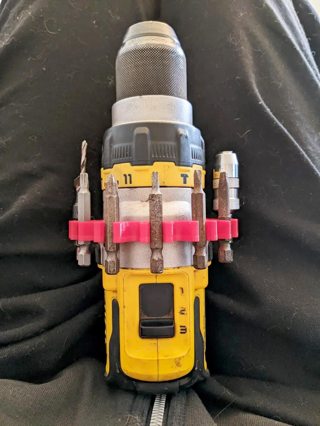 Top view of a yellow drill with a 3D-printed bit holder clip securely attached, organizing various drill bits.