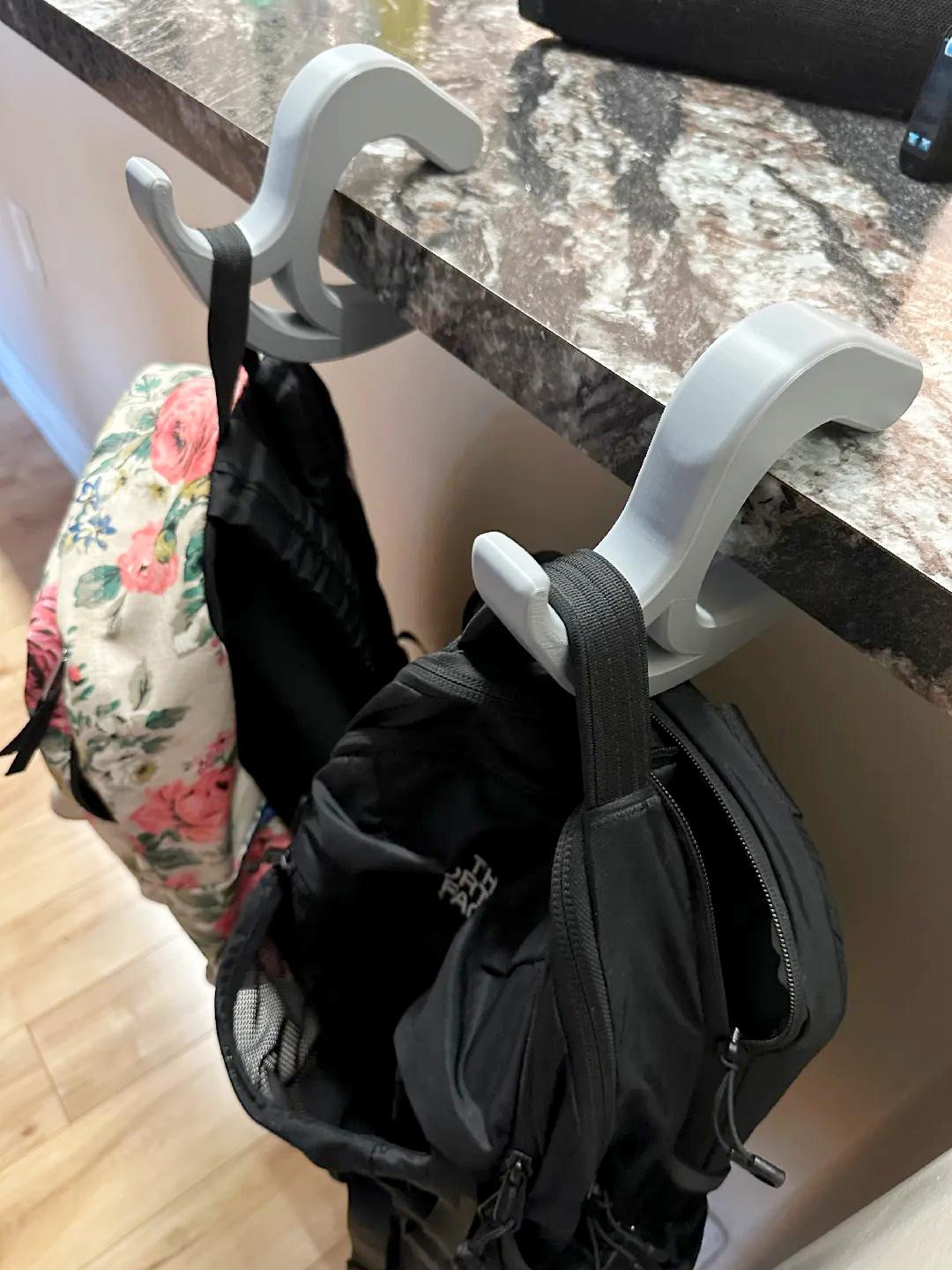 Portable desk bag hooks holding backpacks on a countertop, showcasing a convenient workspace accessory.