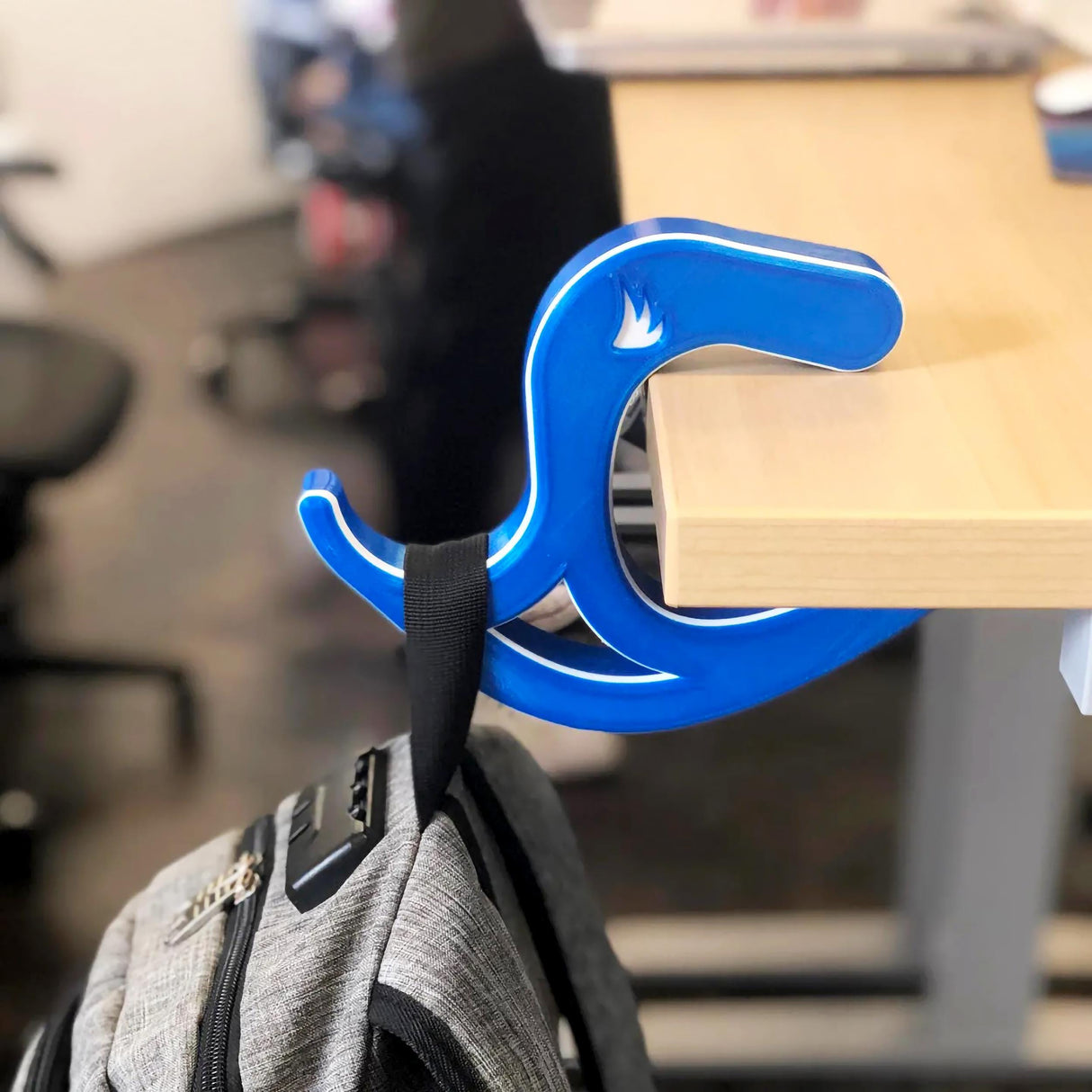 Blue desk bag hook holding a backpack, keeping bags off the floor and organized at a desk.