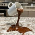 Floating spilling coffee cup sculpture creating an optical illusion on a kitchen countertop.
