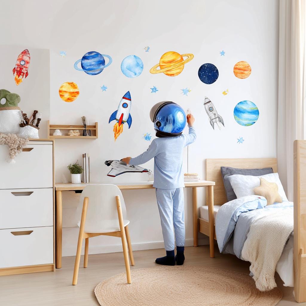 Child in astronaut helmet with watercolor planet and rocket wall decals in a bright kids room, inspiring creativity and imagination.