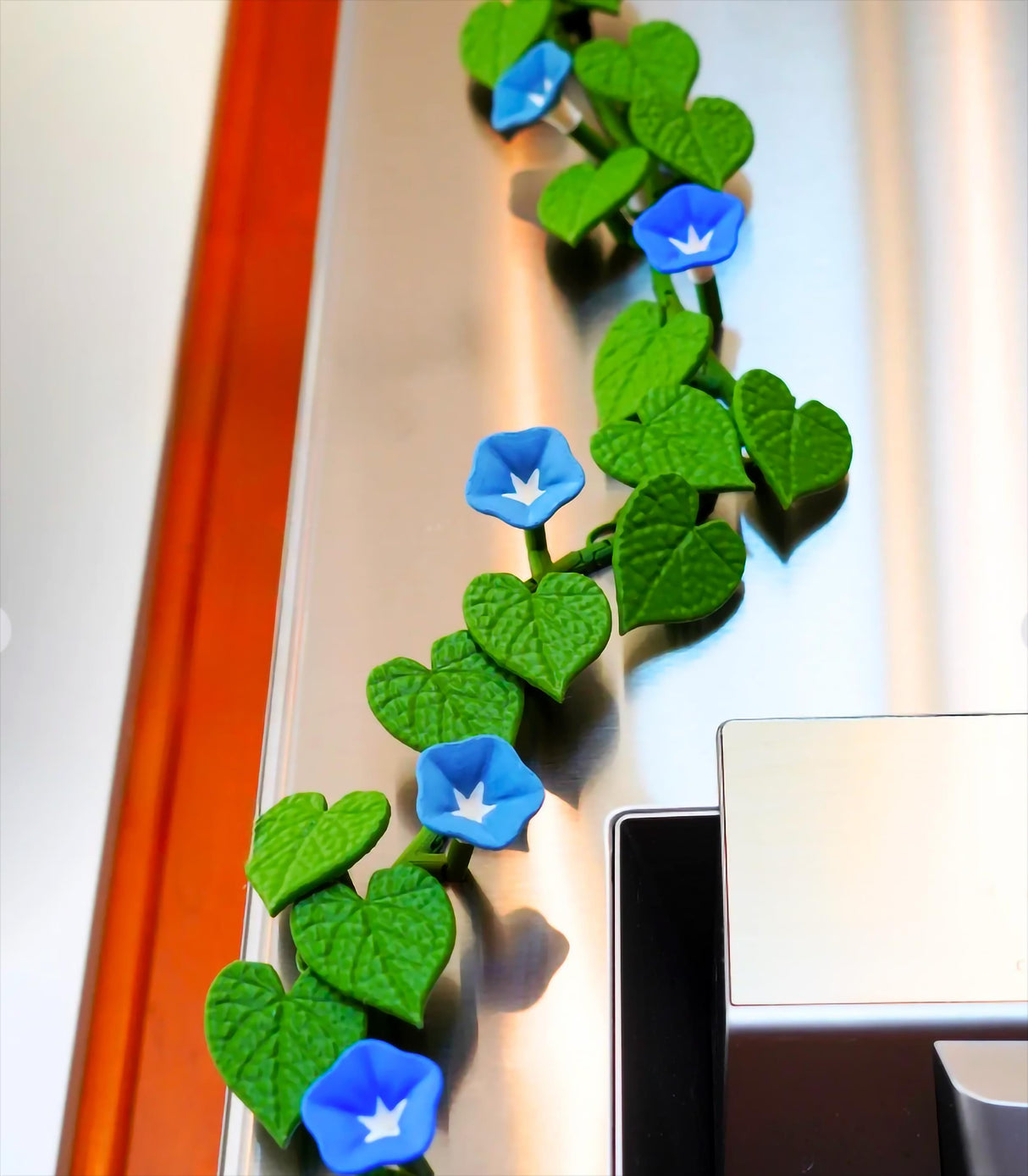 Morning Glory fridge magnets with blue flowers and green ivy leaves on a stainless steel fridge.