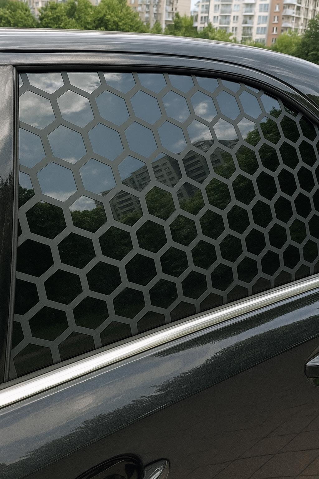 Black car window with matte black honeycomb vinyl decal applied; geometric hexagonal pattern overlaying tinted glass in a sleek, symmetrical design.