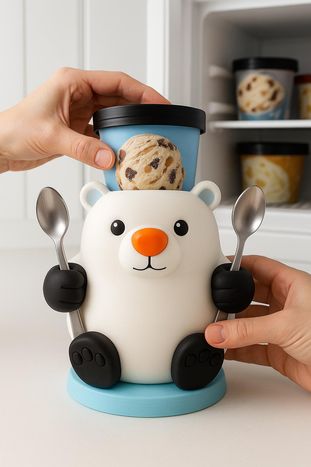 A 3D printed polar bear ice cream holder with a bright orange nose, holding two metal spoons in its paws, with a pint of ice cream on top and a built-in handle on the back. The bear sits on a blue base on a kitchen counter, with a freezer in the background.