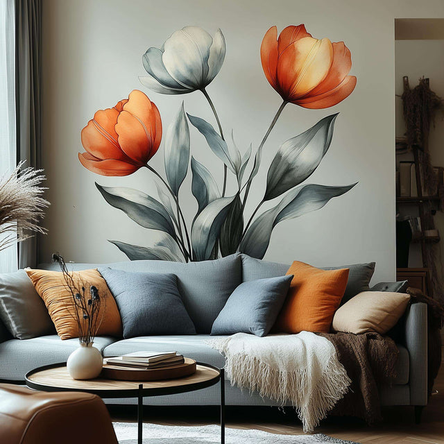 Three large watercolor tulips—two in warm red-orange tones and one in pale ivory—displayed as a wall decal behind a modern light gray sofa with blue and orange accent pillows.