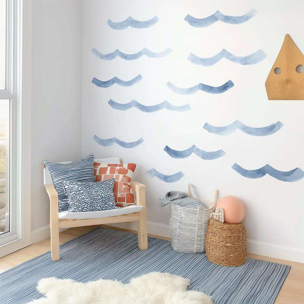Watercolor wave wall decals in varying shades of blue arranged on a white wall above a cozy chair and storage baskets in a coastal-themed kids' room.