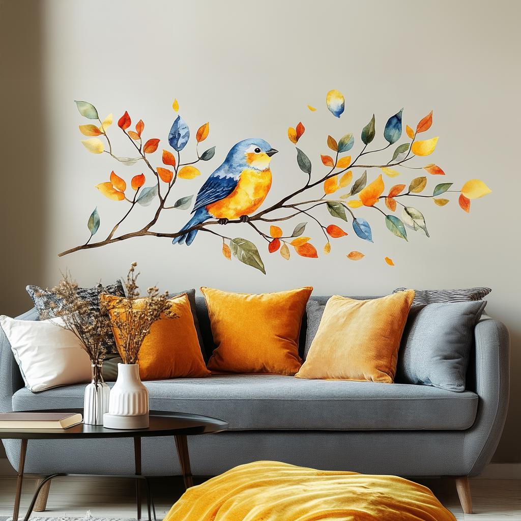 Vinyl wall decal of a watercolor-style bird sitting on a branch with colorful autumn leaves, applied to a light-colored wall above a grey sofa with orange and yellow pillows.