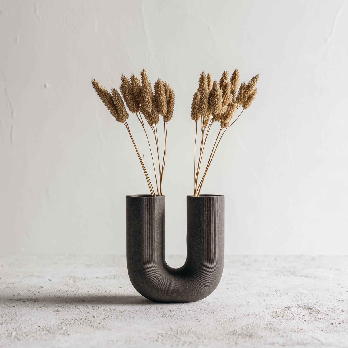 Dark U-shaped 3D printed vase with ribbed texture, styled with dried grasses for illustration; flowers are not included.