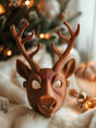 3D printed reindeer mask with sculptural antlers placed near a decorated Christmas tree, modern festive cosplay and holiday decor accessory