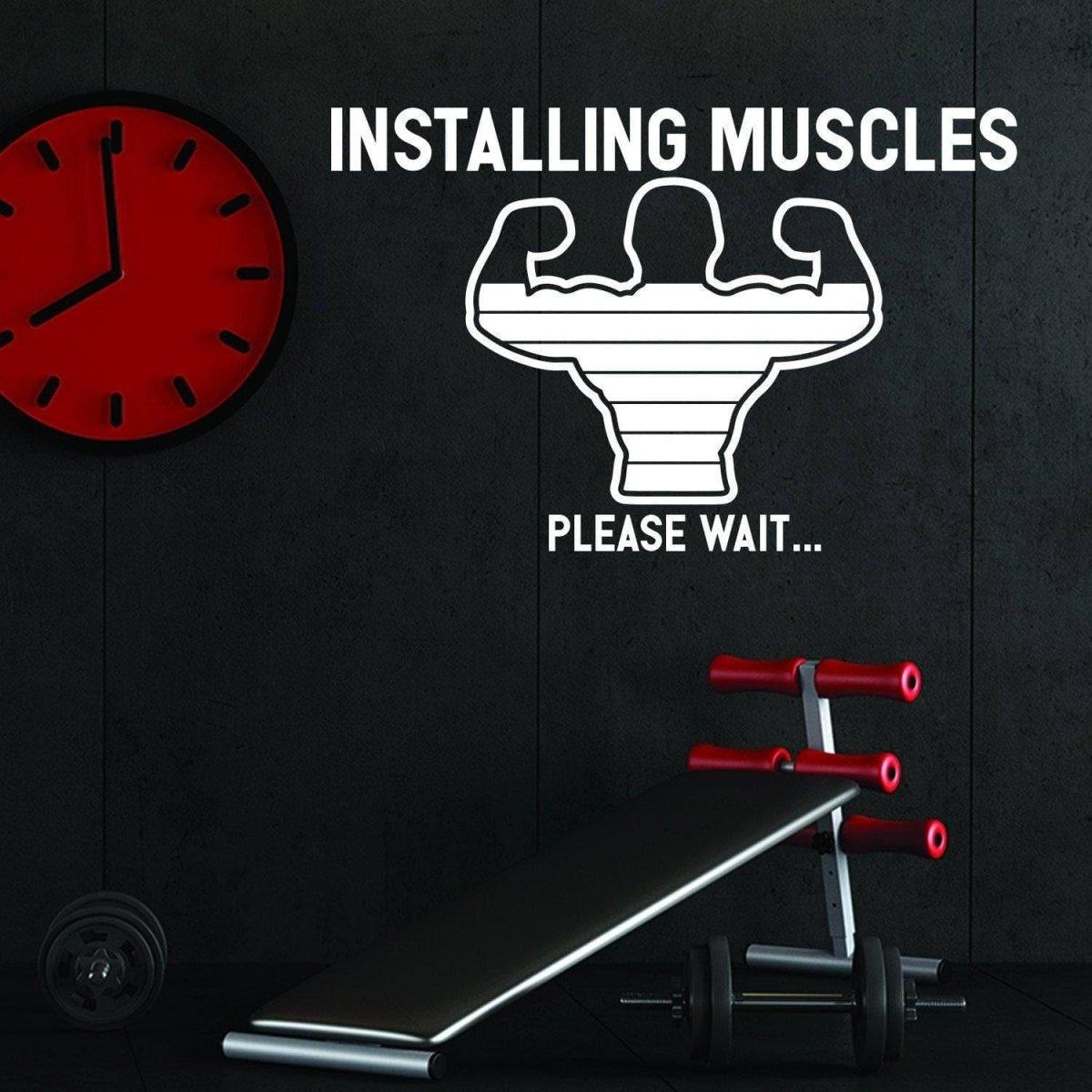 Motivational fitness wall decal 'Installing Muscles, Please Wait...' in a gym setting with weights and clock.