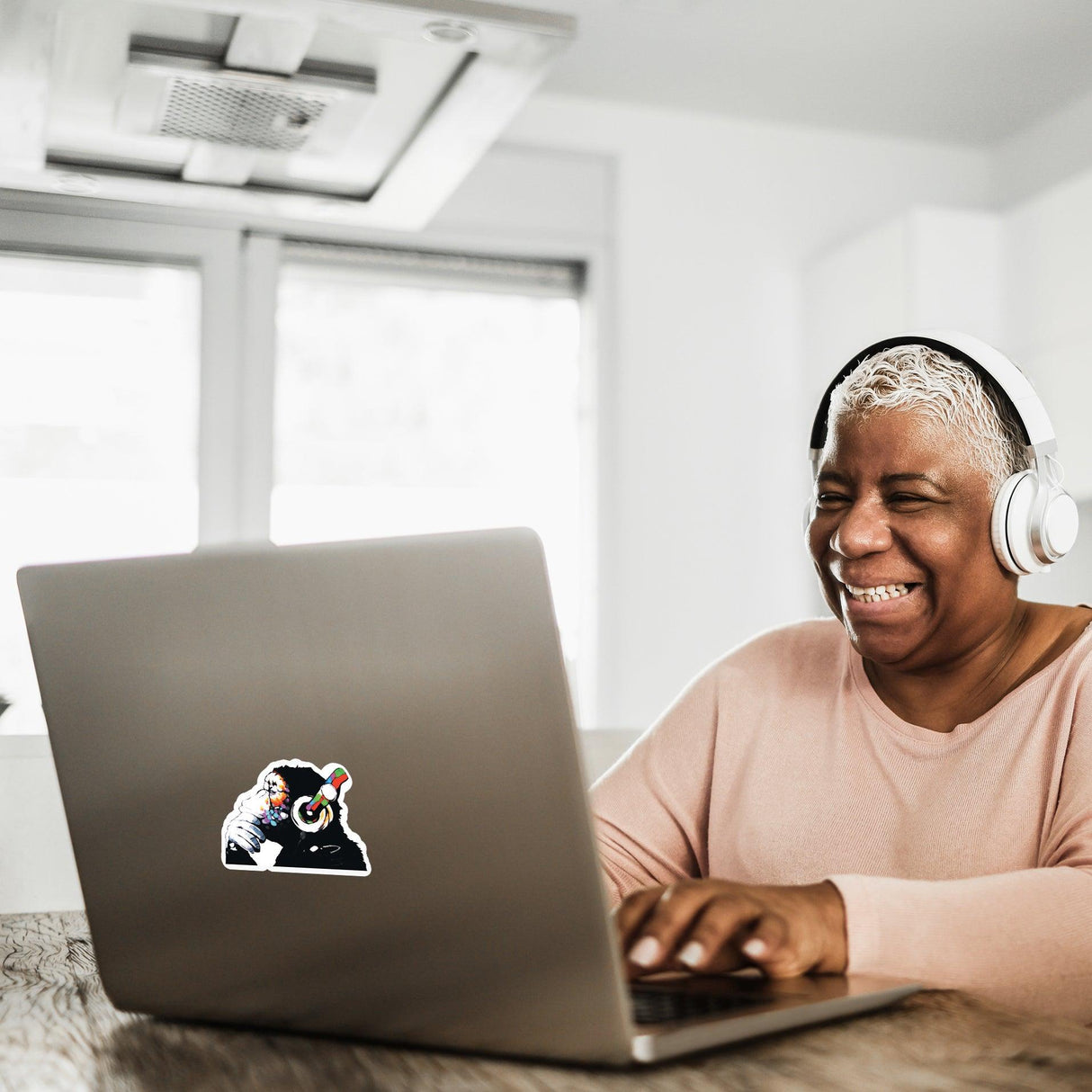 Happy woman with headphones laughing while using a laptop with a music monkey vinyl sticker on it.