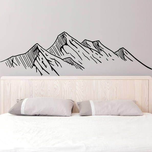 Mountain silhouette wall decal above a bed with decorative pillows, adding a nature-inspired touch to interior decor.